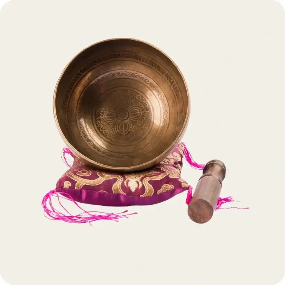 Handcrafted antique singing bowl with intricate design, resting on a decorative cushion, accompanied by a wooden striker.