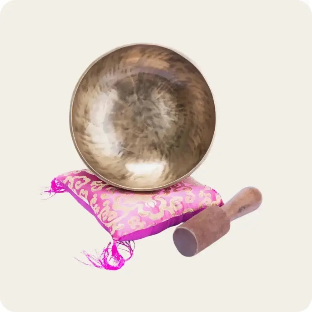 Handcrafted Healing Singing Bowl on a pink cushion with a wooden striker, used for meditation and sound therapy.